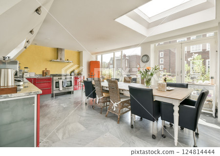 A stylish modern kitchen featuring a spacious dining area, large windows allowing natural light, and contemporary decor in a vibrant setting. 124814444