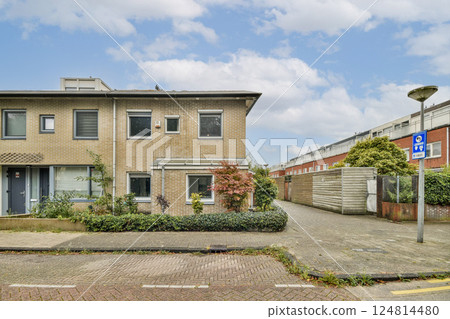A modern residential building features large windows and greenery around it, creating a welcoming environment. The clear sky adds to the serene ambiance. A modern residential building features large windows and greenery around it, creating a welcoming environment. The clear sky adds to the serene ambiance. 124814480