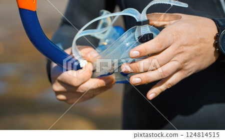 A man holds a mask and snorkeling tube for swimming in the ocean on a sunny day. 124814515
