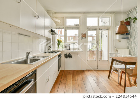 A bright and airy modern kitchen featuring minimalist design, wooden flooring, and natural light flowing through large windows, creating an inviting atmosphere. 124814544
