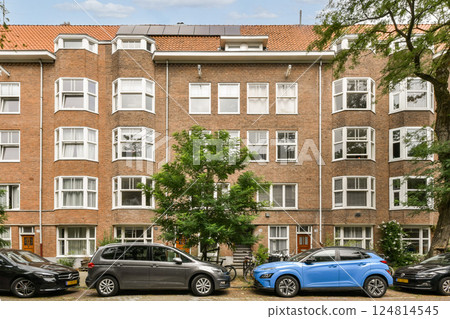 A picturesque urban scene featuring a classic apartment building surrounded by lush trees and parked cars, showcasing modern city life and architecture. 124814545