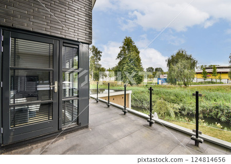 A contemporary balcony features glass railings with a view of lush trees and greenery, highlighting a peaceful outdoor atmosphere. 124814656