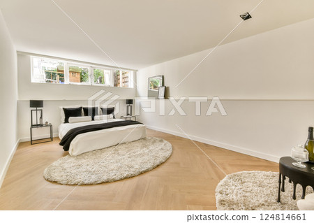 A sleek and stylish bedroom showcasing a modern design featuring soft textures, a cozy rug, and natural light filtering through a large window. A sleek and stylish bedroom showcasing a modern design featuring soft textures, a cozy rug, and natural light filtering through a large window. 124814661