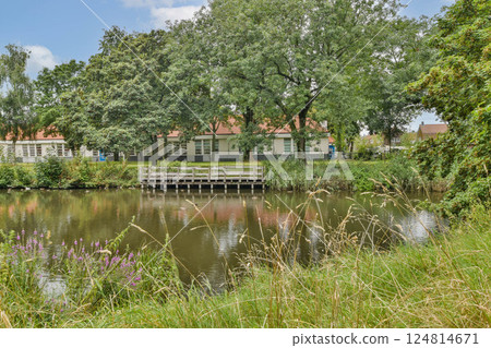 A tranquil lakeside vista featuring vibrant greenery, reflecting water, and wooden bridge, inviting peaceful contemplation in nature's embrace. A tranquil lakeside vista featuring vibrant greenery, reflecting water, and wooden bridge, inviting peaceful contemplation in nature's embrace. 124814671