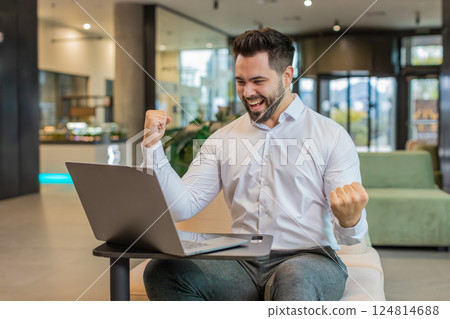 Caucasian bearded businessman working on laptop shocked by sudden victory in modern hotel lobby Caucasian bearded businessman working on laptop shocked by sudden victory in modern hotel lobby 124814688