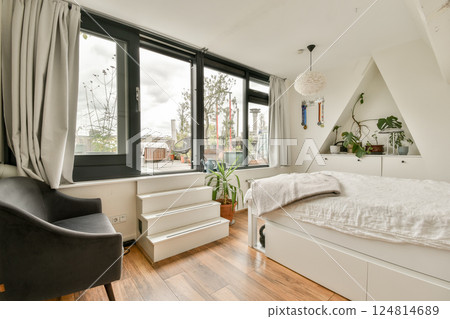 A modern, minimalist bedroom featuring large windows, cozy bedding, and a stylish chair. Natural light fills the space, enhancing the relaxed atmosphere. A modern, minimalist bedroom featuring large windows, cozy bedding, and a stylish chair. Natural light fills the space, enhancing the relaxed atmosphere. 124814689