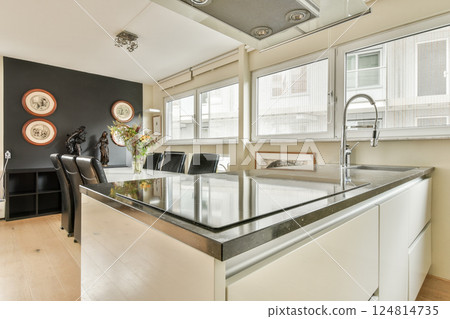 A sleek modern kitchen showcasing minimalist design elements with a dark accent wall and stylish decor. The space features a prominent island and contemporary appliances. 124814735