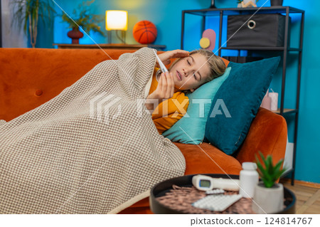 Teenager boy sick with fever lying on sofa checking high temperature on thermometer sad tired home 124814767