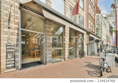 The image showcases a modern building facade with large glass windows, an appealing entrance, and urban elements, typical of contemporary architecture. 124814768