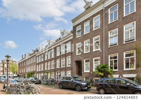 A picturesque street showcasing traditional Dutch architecture with elegant brick buildings and lush greenery along the canal. Bicycles line the pathway, enhancing the local charm. A picturesque street showcasing traditional Dutch architecture with elegant brick buildings and lush greenery along the canal. Bicycles line the pathway, enhancing the local charm. 124814803