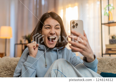 Woman on sofa using smartphone happily jumping and shouting with joy celebrating victory in game 124814812