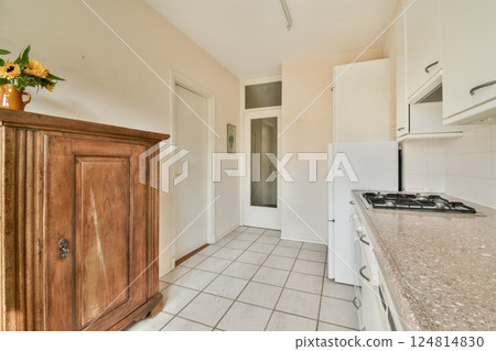 A well-lit kitchen featuring wooden cabinetry, a modern countertop, and tiled flooring, offering a cozy and functional cooking space. A well-lit kitchen featuring wooden cabinetry, a modern countertop, and tiled flooring, offering a cozy and functional cooking space. 124814830