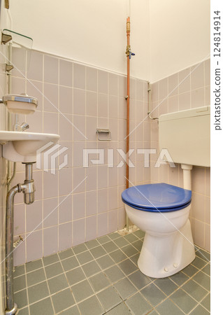 A clean, minimalist bathroom featuring a toilet and sink against tiled walls. The layout emphasizes functionality and a spacious feel. 124814914