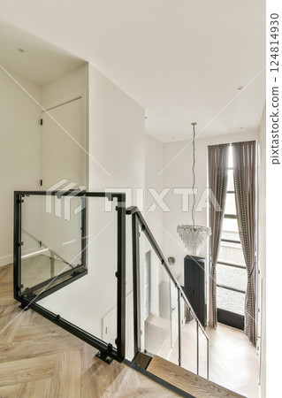A contemporary interior showcasing an elegant staircase adorned with glass railings, featuring a chic chandelier and stylish curtains. 124814930