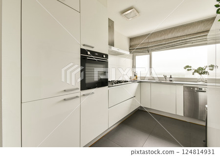 Sleek white cabinetry with modern appliances, large windows offering natural light, and a contemporary aesthetic define this elegant kitchen space. Sleek white cabinetry with modern appliances, large windows offering natural light, and a contemporary aesthetic define this elegant kitchen space. 124814931