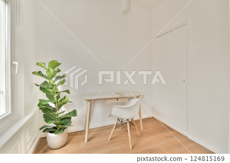 A serene and bright interior featuring a simple wooden desk, a modern chair, and a leafy plant by the window, creating a calming atmosphere. 124815169