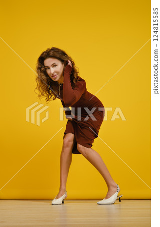 Woman poses playfully in a stylish outfit against a bright yellow backdrop in a studio Woman poses playfully in a stylish outfit against a bright yellow backdrop in a studio 124815585