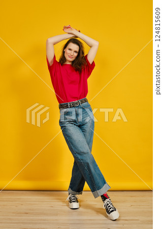 Cheerful adult woman posing in casual outfit against vibrant yellow background 124815609