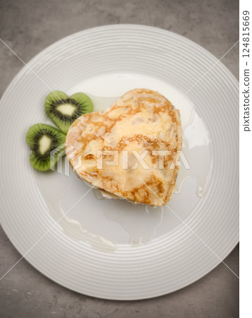 Heart shaped crepes, pancakes served with sliced kiwi fruit and honey on white plate, delicious breakfast or brunch for Mother's Day Valentines copy space 124815669