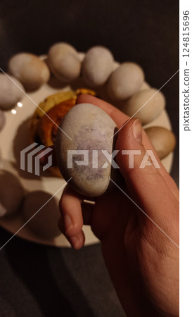 Hand holding a naturally dyed speckled violet carcade easter egg with more eggs and a sweet bread on a plate in background Hand holding a naturally dyed speckled violet carcade easter egg with more eggs and a sweet bread on a plate in background 124815696