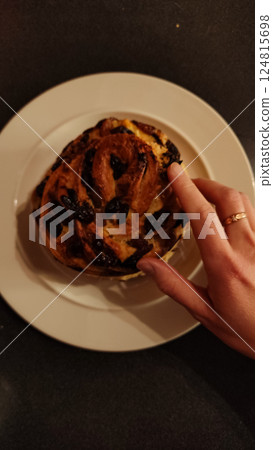 Golden crossed ringed hand touching rustic easter bread with chocolate, raisins on white ceramic plate copy space Golden crossed ringed hand touching rustic easter bread with chocolate, raisins on white ceramic plate copy space 124815698