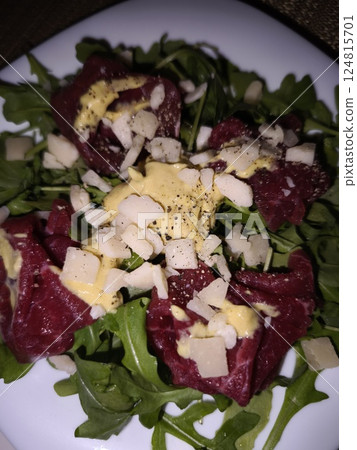 Delicious beef carpaccio served on fresh rocket salad, topped with parmesan cheese and a vibrant mustard dressing, enjoyed in prague. Ideal for parties, buffets, and stylish aperitifs 124815701