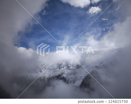 Snow covered mountains in chamonix, france, clouds under a blue sky, creating a dramatic natural scene 124815730