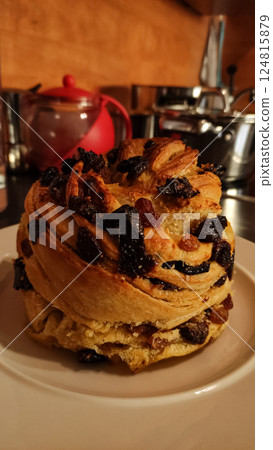 Freshly baked easter bread, adorned with raisins and candied fruit, sits on a white plate, ready to be enjoyed on kitchen table 124815879