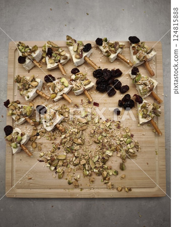 Delicious christmas appetizer idea featuring brie cheese, pistachios, cranberries and pretzel sticks on a wooden cutting board. Ideal for parties, buffets, and stylish aperitifs 124815888
