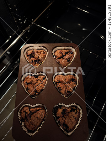 Freshly baked heart shaped blueberry muffins warming inside dark oven, releasing sweet fragrance and filling kitchen with homey comfort for Mother's Day Valentines copy space 124815891