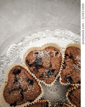 Delicious heart shaped blueberry muffins freshly baked and sprinkled with icing sugar, resting on an elegant glass plate for Mother's Day Valentines copy space Delicious heart shaped blueberry muffins freshly baked and sprinkled with icing sugar, resting on an elegant glass plate for Mother's Day Valentines copy space 124815898
