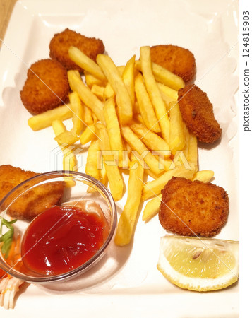 Crispy golden chicken nuggets alongside french fries, garnished with ketchup and lemon wedge on pristine white ceramic plate 124815903