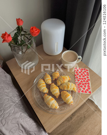 Valentine's day breakfast with fresh croissants, coffee, red roses, and a heart patterned napkin on a bedside table 124816106