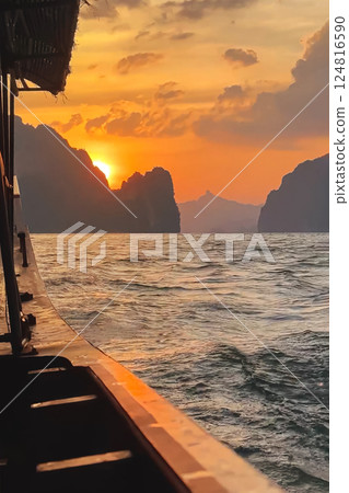 An incredible sunset on Cheo lan Lake view from a longtail boat floating on the lake. The orange sun over the mountains in Khao Sok Park in Thailand, vertical photo. An incredible sunset on Cheo lan Lake view from a longtail boat floating on the lake. The orange sun over the mountains in Khao Sok Park in Thailand, vertical photo. 124816590