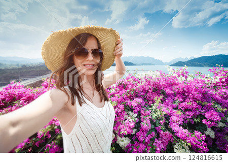 Woman in wide-brimmed straw hat travels alone Thailand, and takes a selfie against background of the Dam at Cheo lan Lan Lake in Khao Sok Park against the background of the reservoir, mountains and 124816615