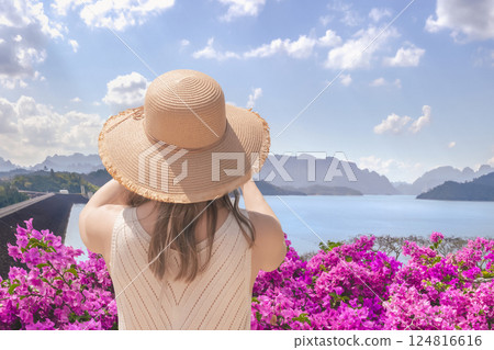 Woman tourist traveler in a wide-brimmed hat takes pictures of Lake Checo Lan and Dam from viewing point, rear view. Thai Tourist Spots such as Rachaphrapha Dam in Khao Sok Park in Phang Nga Province 124816616