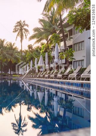 A pool under palm trees in a tropical climate. Rows of sun beds along the pool and covered umbrellas. Morning in a luxury hotel, a paradise for relaxation A pool under palm trees in a tropical climate. Rows of sun beds along the pool and covered umbrellas. Morning in a luxury hotel, a paradise for relaxation 124816638