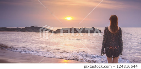 Panorama of the Sunset in Thailand. A woman in a black beach dress looks at the setting sun on a stone ridge in the sea on the beach in Kaolak, relaxing and admiring nature. 124816644