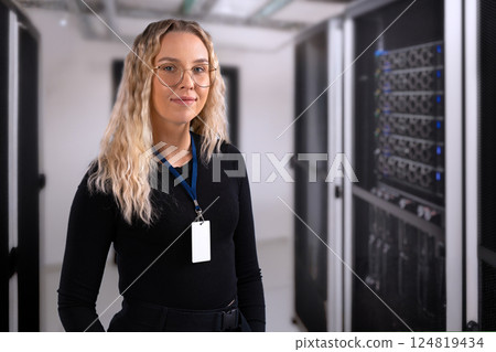 Female IT professional in datacenter with confident expression wearing security identification badge. IT consultant in server and network room 124819434
