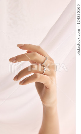 Cropped image of tender female hand with manicured nails wearing two delicate rings against a softly draped white fabric. Cropped image of tender female hand with manicured nails wearing two delicate rings against a softly draped white fabric. 124820169
