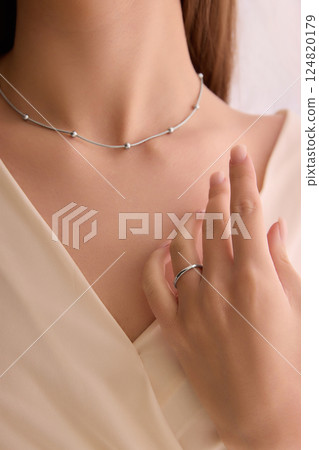 Cropped image of young woman wearing delicate silver necklace with small spherical accents and a simple ring. Cropped image of young woman wearing delicate silver necklace with small spherical accents and a simple ring. 124820179