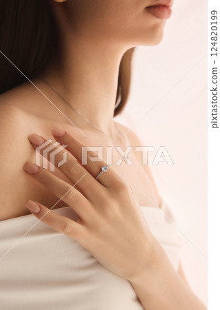 Cropped side view portrait of woman with engagement ring and silver necklace, radiating soft beauty and romantic charm 124820199