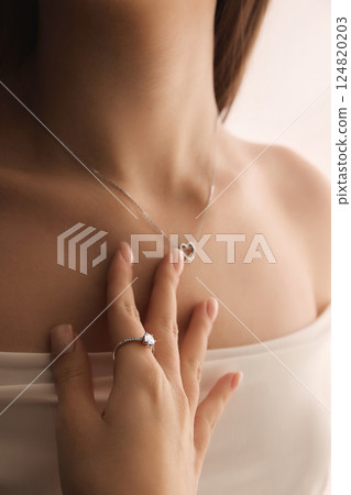 Close-up of woman hand with diamond engagement ring gently holding heart pendant on neck. Close-up of woman hand with diamond engagement ring gently holding heart pendant on neck. 124820203