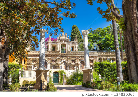 The Alcazar of Seville, historic royal palace in Seville town, Andalusia, Spain. Ornate palace architecture framed by lush greenery and classical columns on a sunny day. 124820365