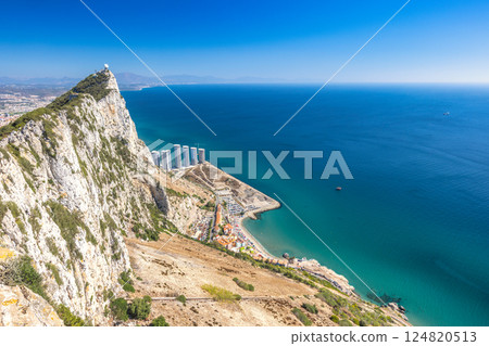 Gibraltar, British Overseas Territory and city on the Iberian Peninsula. Coastal clifftop view overlooking the ocean, buildings, and a distant coastline under a clear blue sky. Gibraltar, British Overseas Territory and city on the Iberian Peninsula. Coastal clifftop view overlooking the ocean, buildings, and a distant coastline under a clear blue sky. 124820513