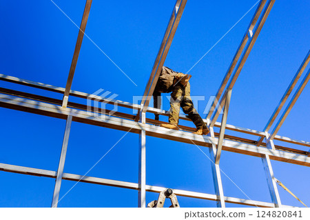 Construction worker is positioned high on steel framework, carefully installing metal beams 124820841