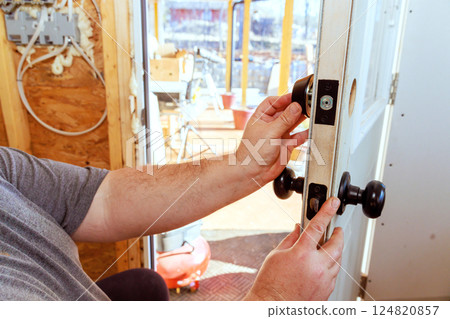 Contractor is carefully installing door lock at works, secure fit during construction Contractor is carefully installing door lock at works, secure fit during construction 124820857
