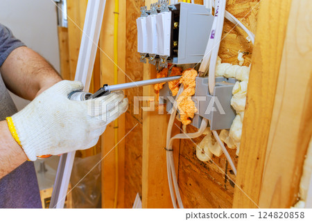 An electrician installs wiring outlets while sealing gaps with spray foam insulation in new home being built. An electrician installs wiring outlets while sealing gaps with spray foam insulation in new home being built. 124820858
