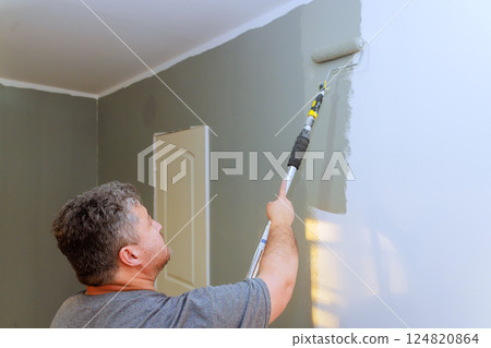 Contractor applies gray paint to wall using roller while standing indoors in good lighting conditions. Contractor applies gray paint to wall using roller while standing indoors in good lighting conditions. 124820864