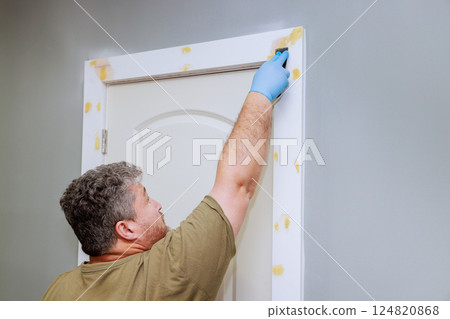 Homeowner works applies wood filler on door trim, using tool while preparing before painting 124820868
